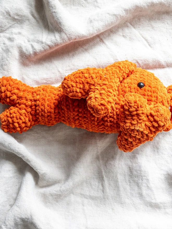 Chunky Chenille Cuddly Crochet Crustacean Lobster Plush, an orange lobster plush sitting on a white table cloth. 