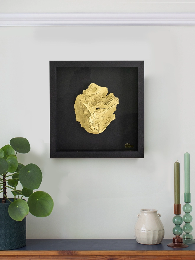 Brass topographical map framed and mounted in black hung on the wall.