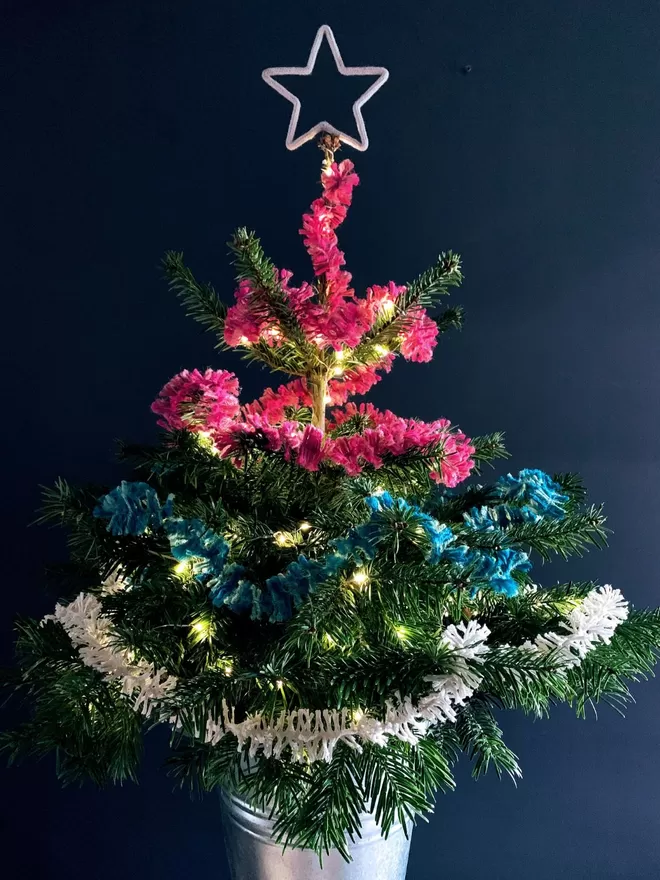 Bright pink jute string tinsel AKA Strinsel on a real Christmas tree against a dark grey wall