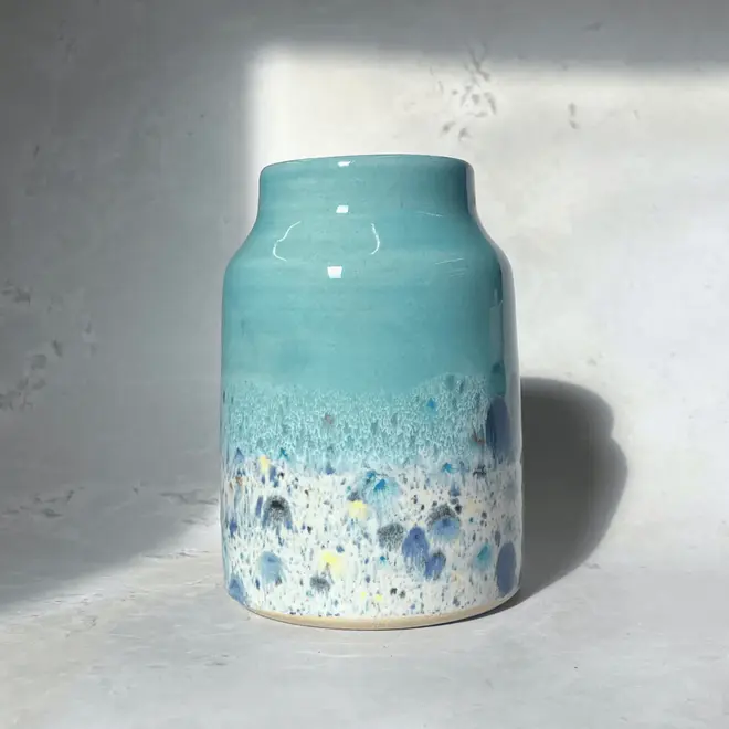 Shoreline Large Vase, a colourful vase placed on a stone surface in front of a plain backdrop. 