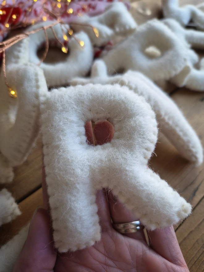 A hand holding a felt letter R. Part of an ivory white Merry Christmas galand.