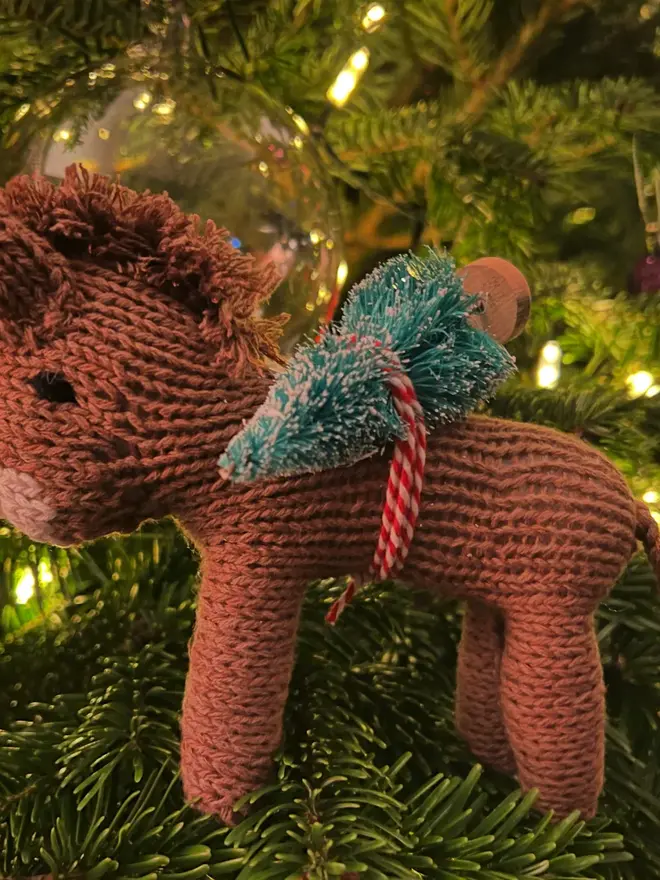 Hand Knitted Natural Dyed Wool And Alpaca Yarn Donkey Gift, a donkey gift sitting in a Christmas tree surrounded by fairy lights. 