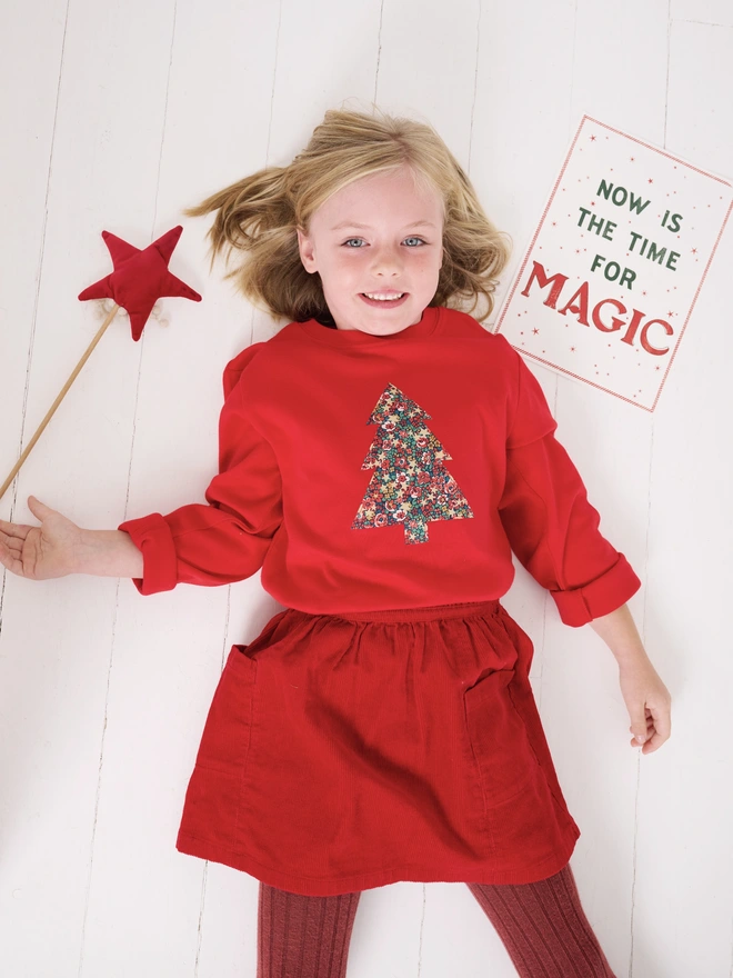 a 5 year old girl wearing a red t-shirt with a liberty floral christmas tree sewn on to the front