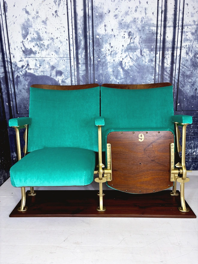 Set of two vintage refurbished cinema seat upholstered in a beautiful green plain velvet.  The cinema seats have gold legs and are mounted onto a wood plinth.  One seat is open and one seat is closed.