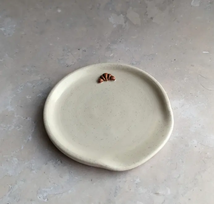 Croissant stoneware spoon rest in vanilla bean glaze against a grey marble background.