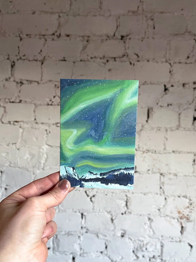a greetings card featuring an illustration of the northern lights above a snowy landscape