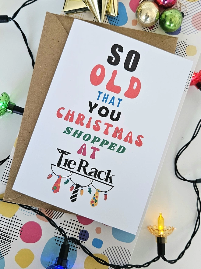 A photograph of the front of a humorous A6 greeting card illustrated using brightly coloured text and the retro shop logo. The text says so old you Christmas shopped at Tie Rack with garland lights 3 ties hanging off them