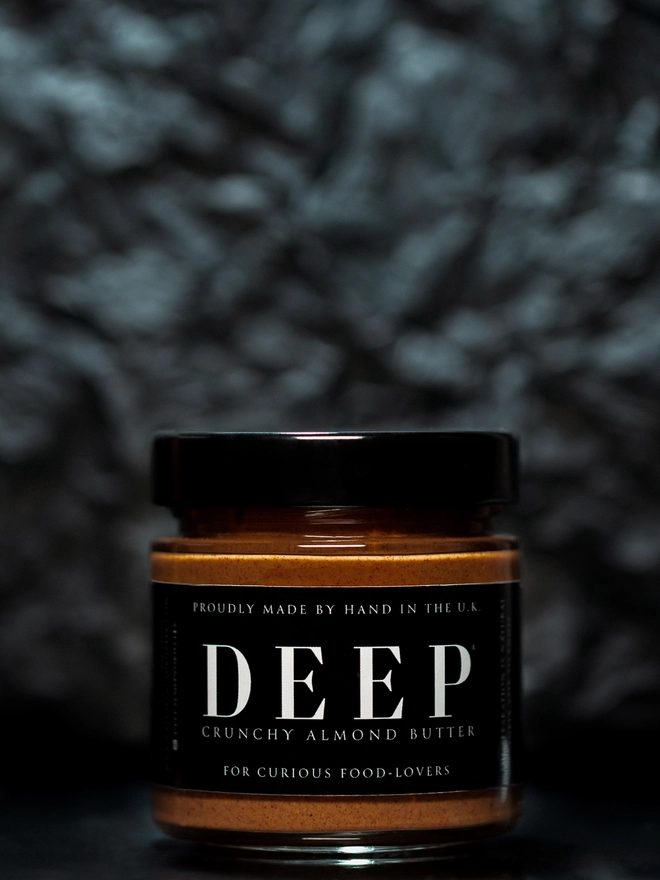 Jar of crunchy almond butter against textured black background