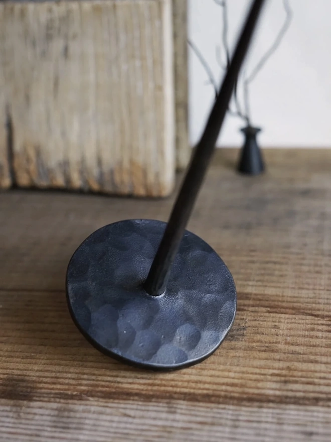 Forged Steel Candle Stick, a metal candle stick sitting on a wooden surface against a wood backdrop. 