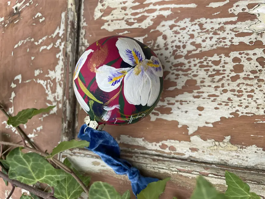 Hand painted floral ceramic christmas bauble dark pink background with Algerian winter iris flowers.