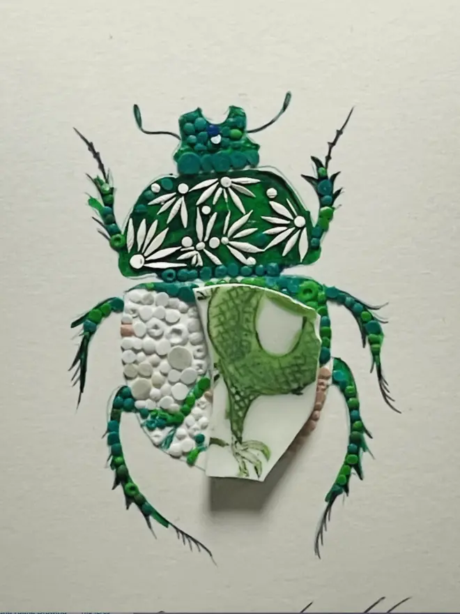 Hand-drawn, painted, mosaic clay, vintage green Dragon pottery insect on white double mounted card, in a black circular frame.