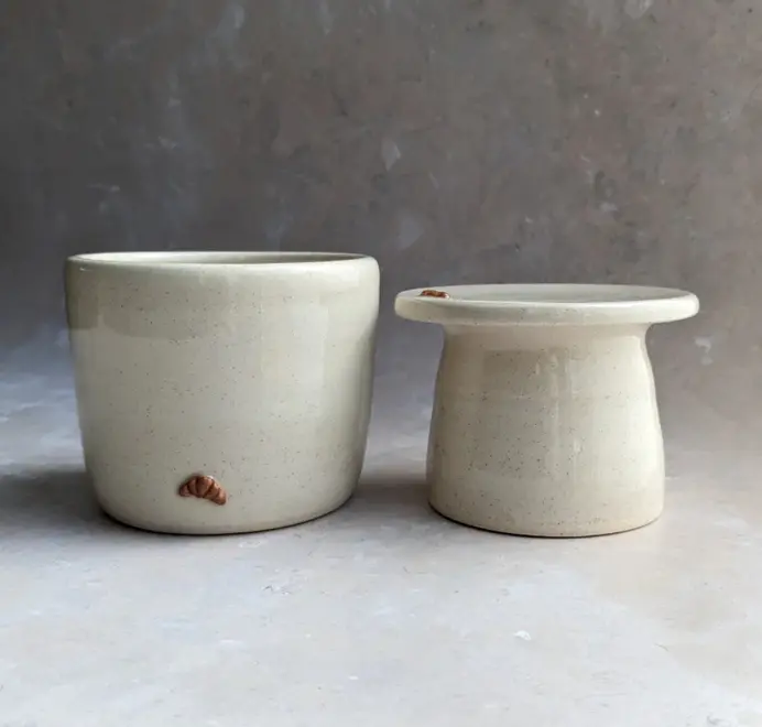 Croissant Butter Crock in vanilla bean glaze with a small croissant design on the front, set against a grey marble background.