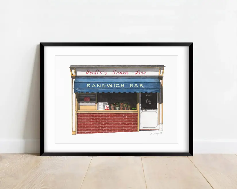 Clerkenwell Scotti's Snack Bar Giclée Print (Unframed), a print of a snack bar sitting in a black frame on a wooden surface against a plain backdrop. 