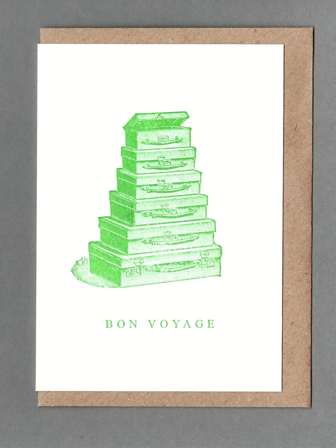 White card with green illustration of a stack of cases and text reading 'Bon Voyage' with a brown envelope behind