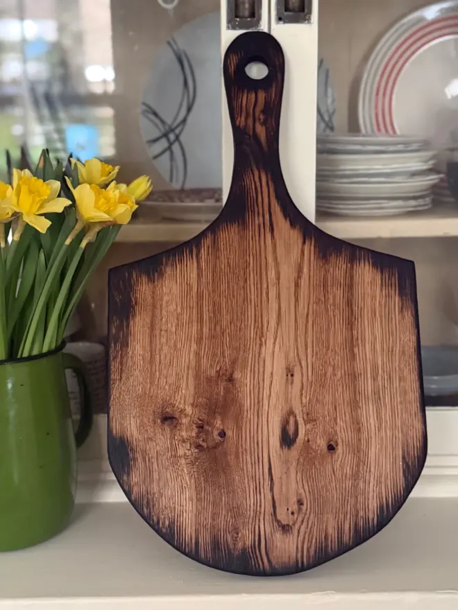 Pizza board styled with backdrop of cream dresser and daffodils showing burnt wood grain