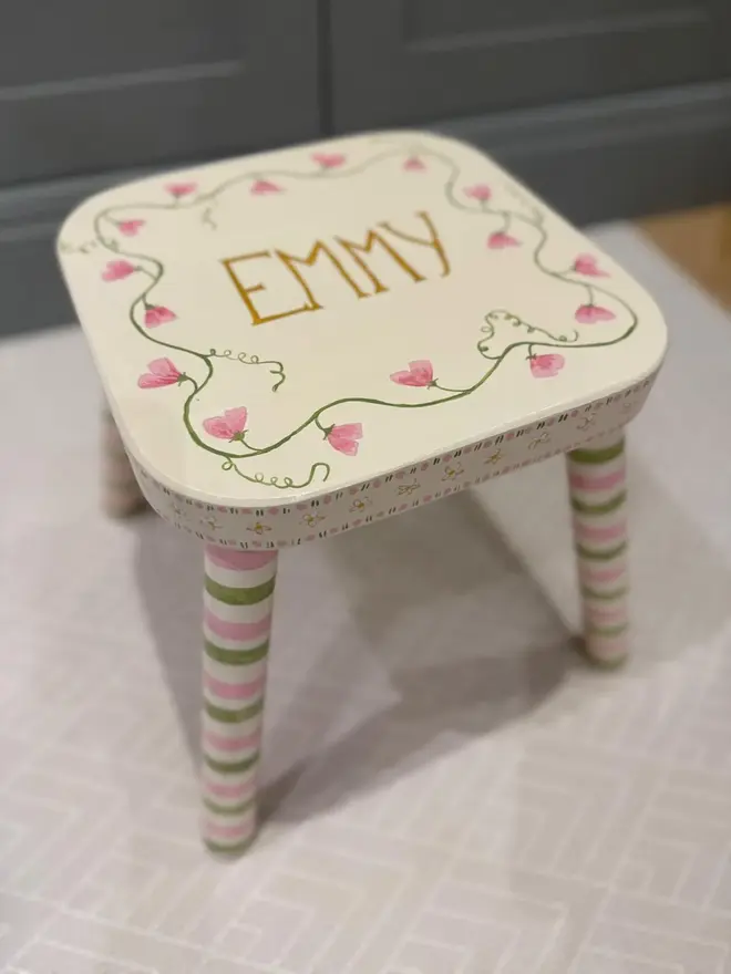 personalised hand-painted nursery stool. a small white stool with green and pink striped legs, painted with 'emmy' on top.