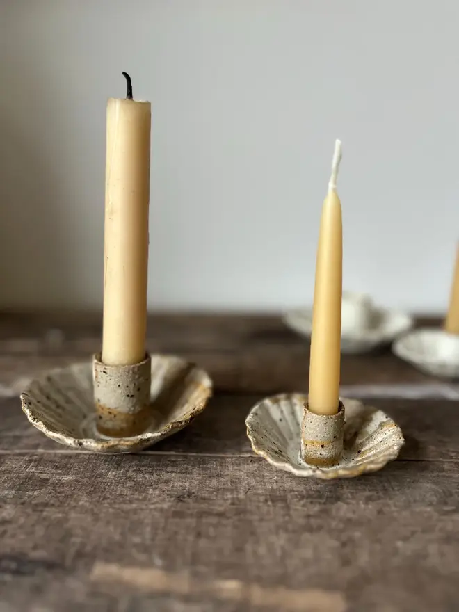 Handmade Natural Speckled Ceramic Candlestick Holder, a group of ceramic candlestick holders sitting on a wooden surface. They are accompanied by some candles. 