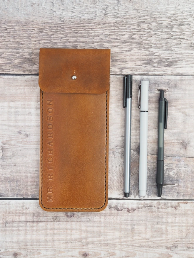 Personalised teachers name leather pencil case. A slim tan brown leather sleeve, designed for pens and pencils. Personalised with a teachers name along the edge.
