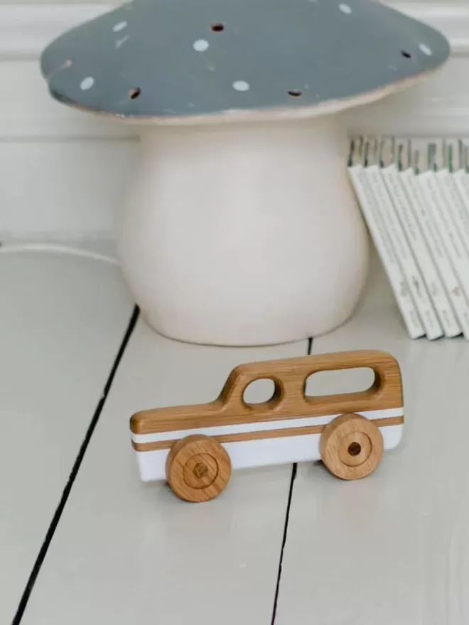 Wooden Toy Car Station Wagon in White on a white wooden floor with a mushroom lamp in the background