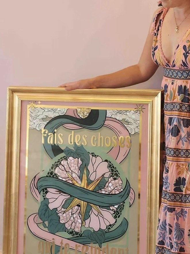'Do Things That Make You Happy' Gold Leaf Glass Artwork, a person standing next to the print, in front of a pink backdrop. 