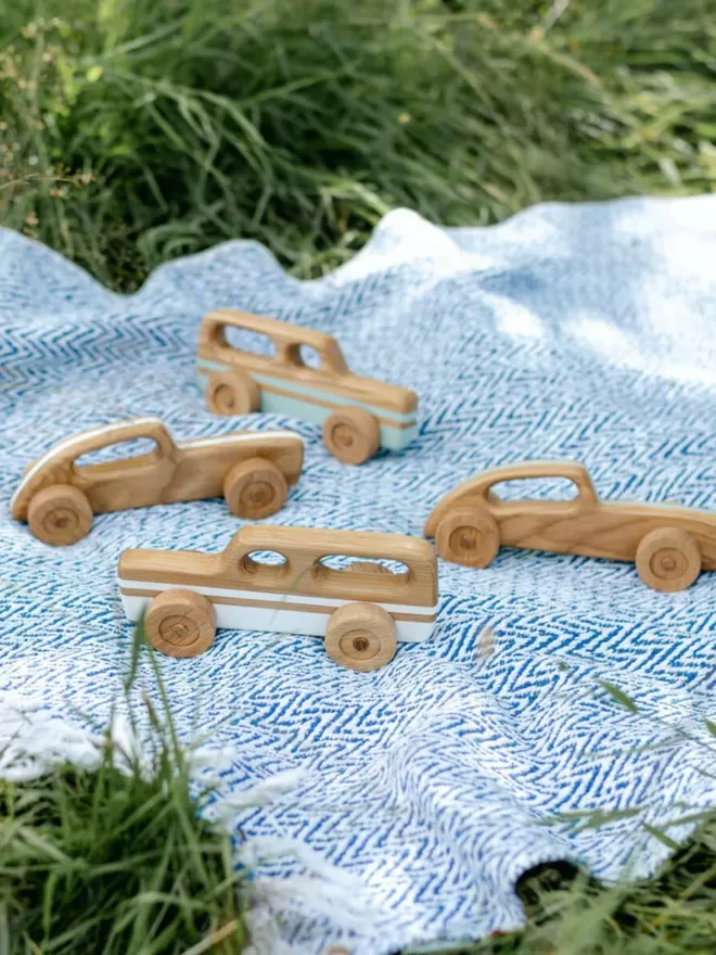 wooden toy racing car amongst 3 other wooden cars on a picnic blanket
