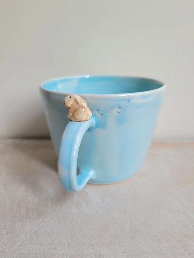 Blue pottery cup with little beige lop eared bunny rabbit on the handle and tiny pawprints