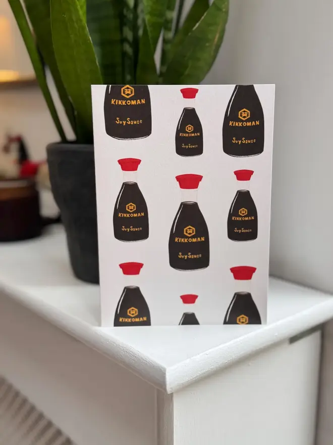 soy sauce bottles illustrated card. card photographed on mantelpiece with houseplant in background.