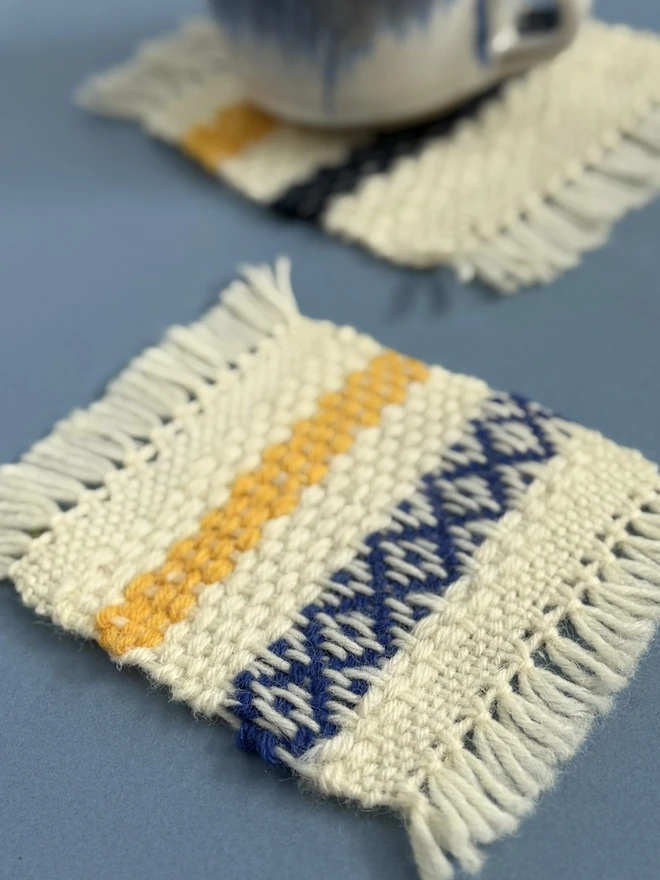 A white blue and mustard wool coaster on a blue background