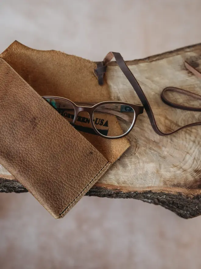 hand stitched leather pouch. a brown leather pouch on a cream cowhide background with a brown strap.