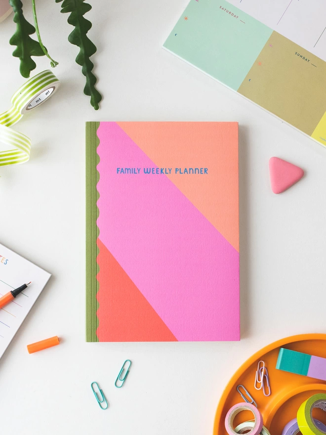colourful pink, rust and peach stripe cover with complimentary olive green wavey spine and hand lettered 'Family Weekly Planner' on the front cover in contrasting blue