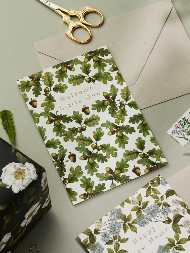 'welcome little one' illustrated oak leaf card. a white card illustrated with oak leaves photographed against a grey background.