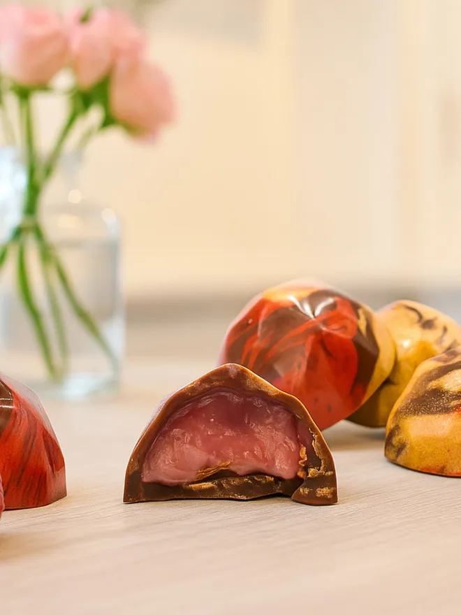 Some luxury milk chocolates with a pink raspberry filling and roses in the background