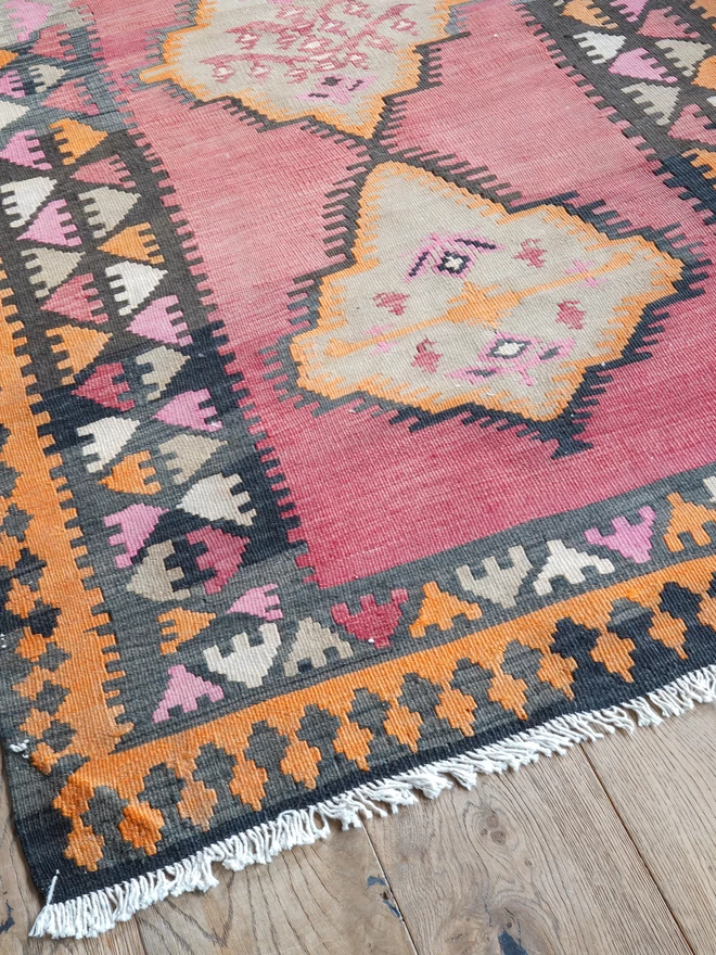 Orangey, red and black geometric vintage kilim hand woven rug on wooden floor in maximalist dining room with green woodwork
