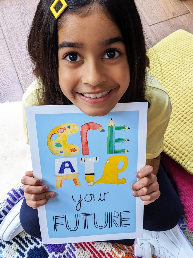 Young girl sitting holding an art print saying 'Create your future'