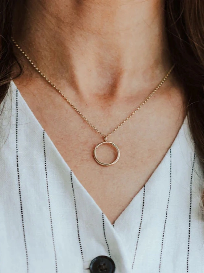 A woman wearing a 9ct Gold open circle necklace wearing a striped shirt