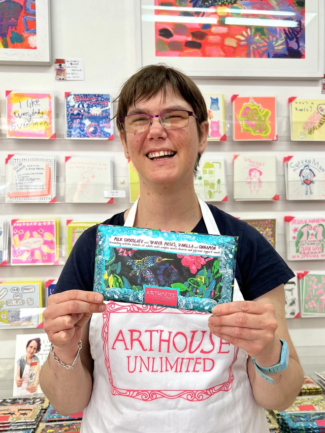Happy artist holding milk charity chocolate bar wrapped in foiled card with a humming bird design