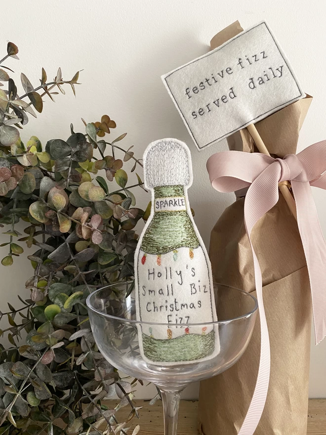 A Little more Christmas Fizz Bottle in a glass with wreath and wrapped bottle  with festive fizz sign