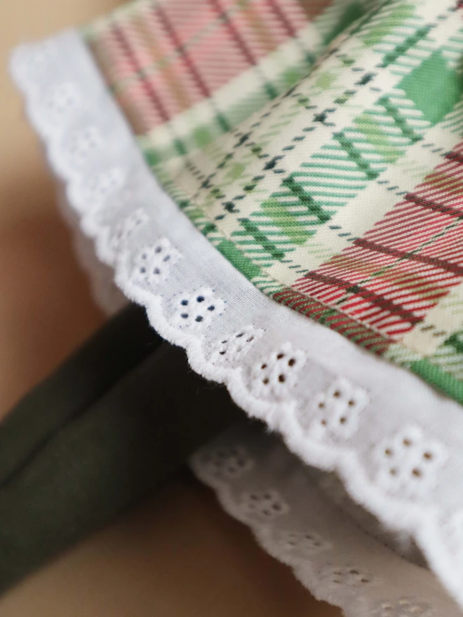 Handmade cloth doll with red brown corduroy hair in a top knot tied with a navy velvet bow, wearing a white textured ruffle collar, a red and green tartan dress with lace trim, and dark green tights.