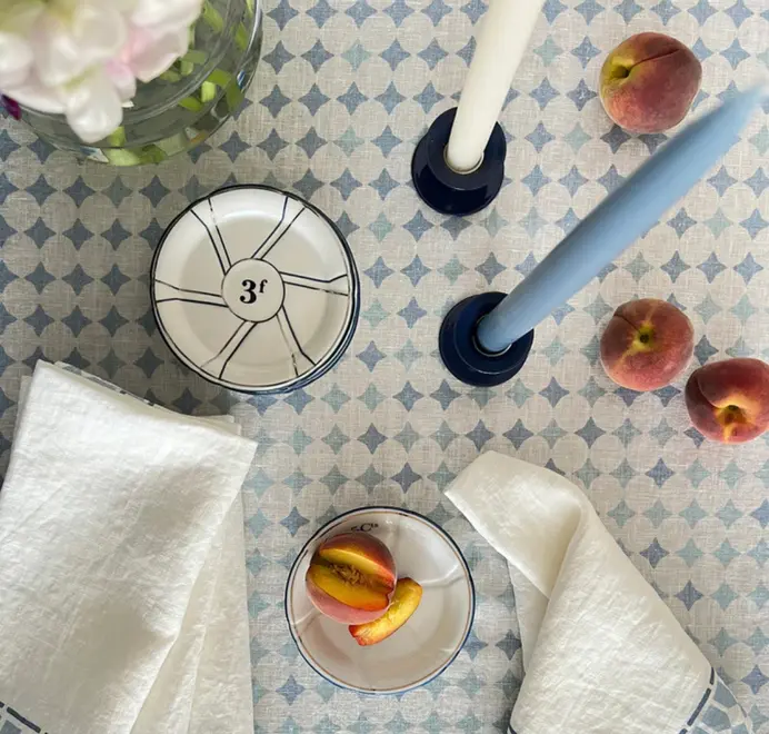 Casa Azul Tablecloth. Blue geometric Casa Azul tablecloth styled with white napkins, ceramic bowls, blue taper candles, and fresh peaches. 