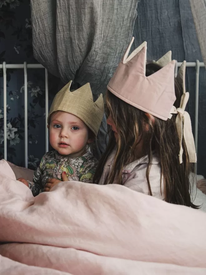 Two children sitting in a bed, one wearing the sparkling Old Gold Crown.