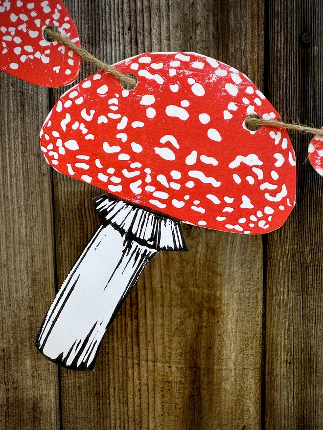 Close up of a Fly Agaric Mushroom. Part of a Hand Printed Garland. A component from a 9 mushroom bunting, printed in red and black Ink. Fungi hanging on brown biodegradable jute string.