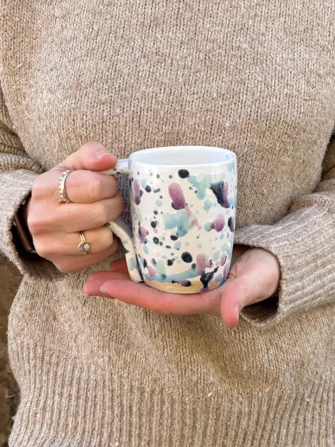 Sweetpea Standard Mug, a woman holding a colourful mug by the handle. 
