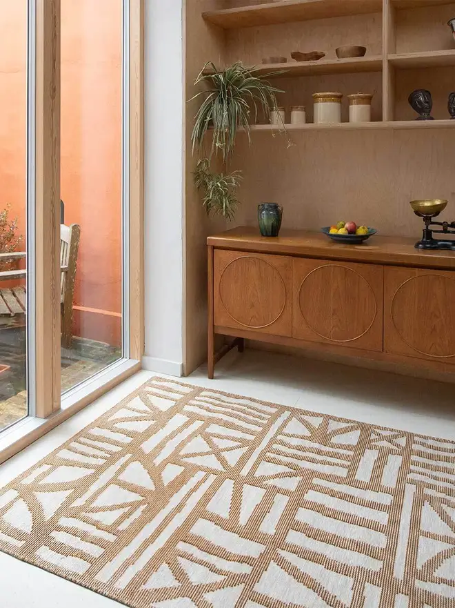 Tudor Flatweave Rug, a colourful rug in a living room. It is surrounded by other household items. 