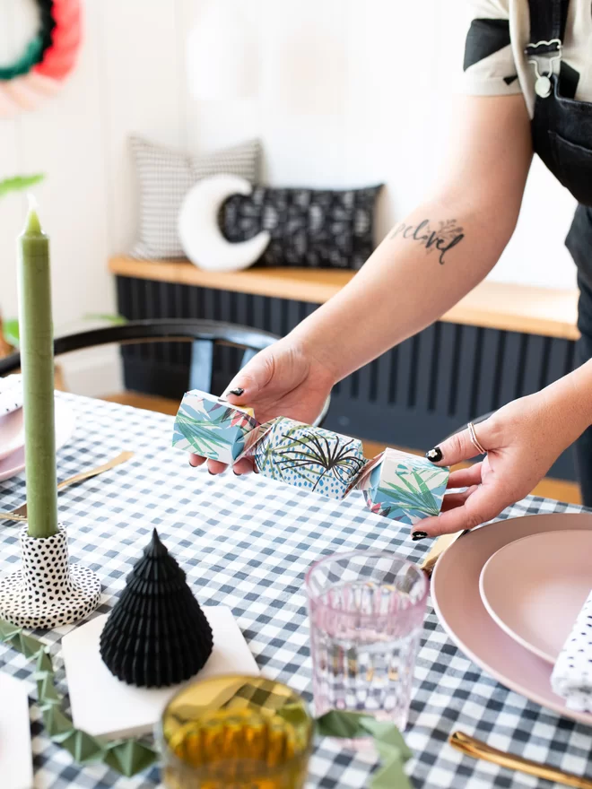 Woman placing an origami cracker on to a place setting for a Christmas dinner party.