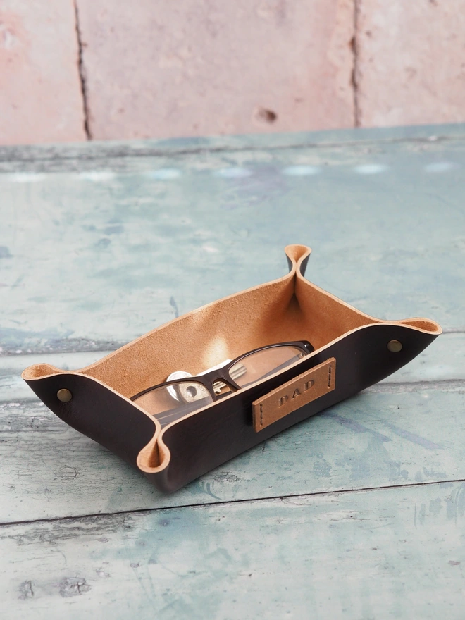 Personalised leather glasses tray. Hand dyed dark brown leather tray holding a pair of reading glasses.