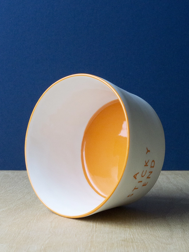 Ceramic porcelain pudding bowl with A Sticky End written on the side. A white pudding bowl with orange rim and interior.
