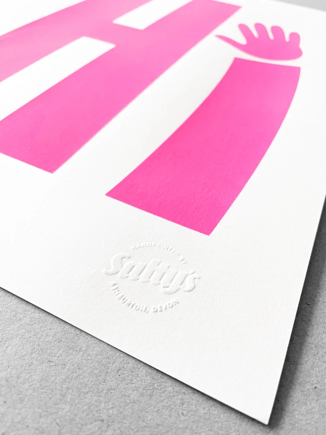 Close up of a neon pink printed Hi upon a white sheet on paper - sat on a grey background. Close up shows the stamp in the bottom right corner