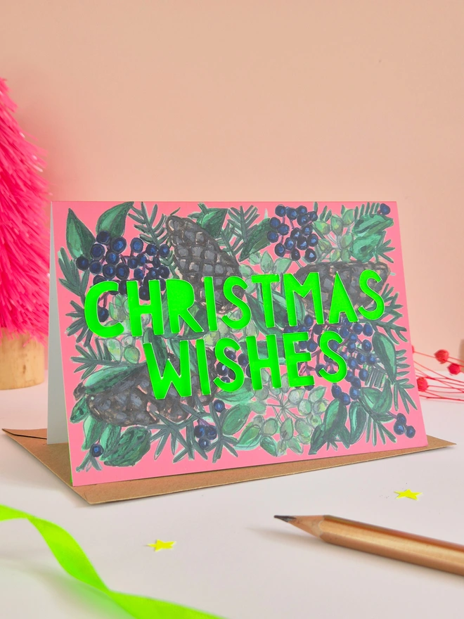 xPine Cone and blue berry illustration card with Christmas Wishes in paper cut text and a neon green backing paper Pine Cone and blue berry illustration card with Christmas Wishes in paper cut text and a neon green backing paper 