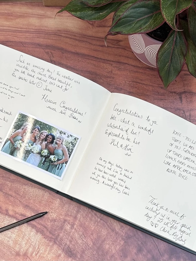 Landscape Personalised Wedding Guest Book covered in Jewel Bookcloth, opened on a wooden surface with photos and writing inside. 
