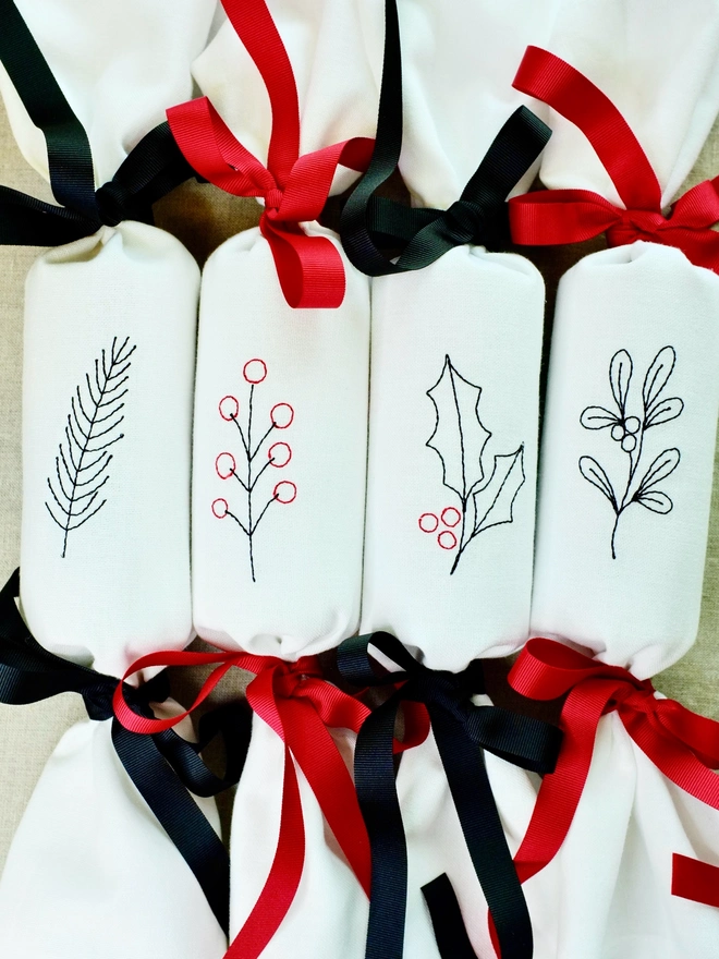 Set of four fabric embroidered Christmas crackers with festive fir, holly, mistletoe, and berry designs, tied with red and black ribbons 